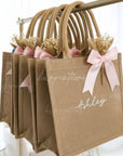 Jute bags with pink bows and personalized names hanging on a rack.