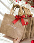 Personalized Jute bags with red ribbons and 'Ashley' text for name personalization, surrounded by Christmas decorations. Handmade by Bossy Creations