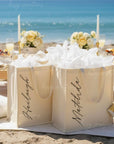 Beachside bridesmaid picnic in pale yellow color theme table setting with personalized gift bags, flowers, and candles by the ocean.