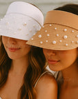 Two women wearing pearl-embellished sun visors on a beach.