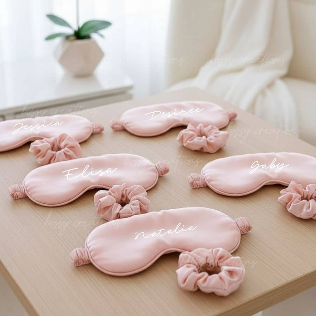 Set of pink eye masks with matching scrunchies on a wooden surface, with a blurred background.