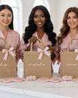 Three women holding personalized bags with names on them, wearing matching robes.