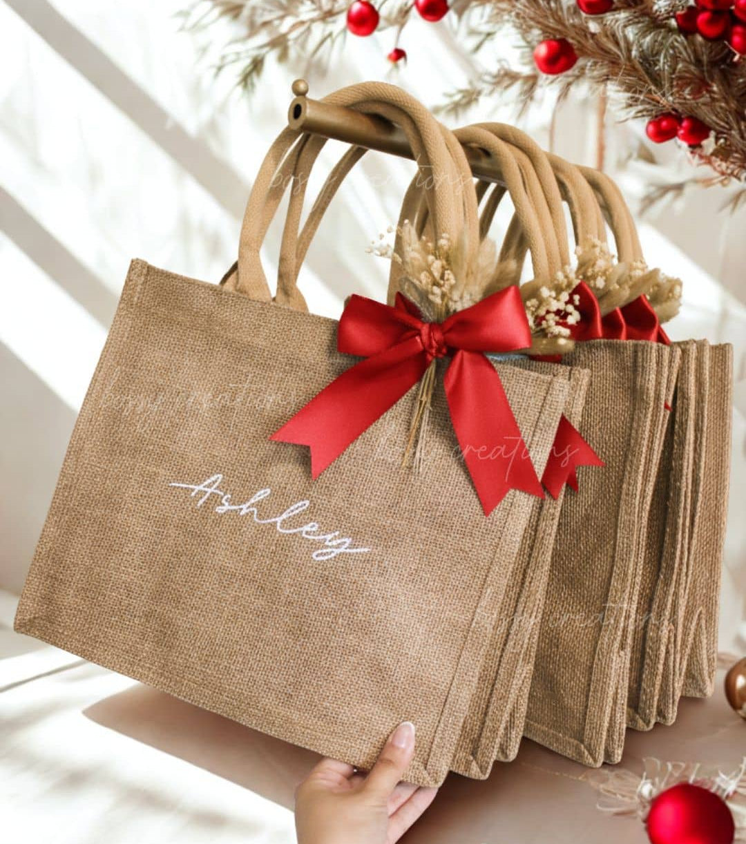 Personalized Jute bags with red ribbons and 'Ashley' text for name personalization, surrounded by Christmas decorations. Handmade by Bossy Creations