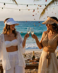 Two women celebrating on a beach with drinks and palm trees.
