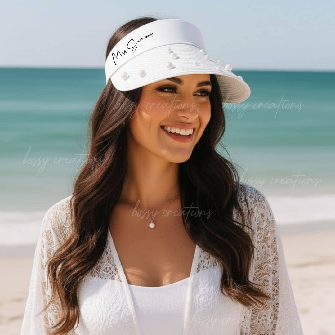 Woman wearing a white visor with 'Mrs. Smith' text on a beach at her bachelorette party.